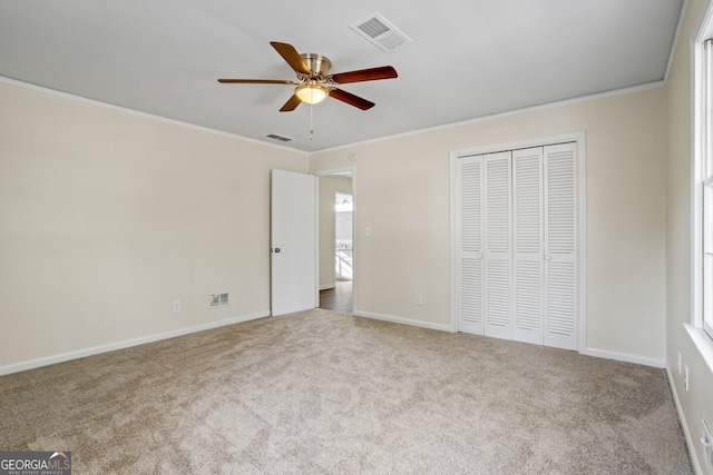 unfurnished bedroom with ceiling fan, light colored carpet, a closet, and crown molding