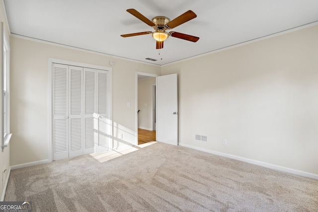 unfurnished bedroom featuring ceiling fan, a closet, light carpet, and crown molding