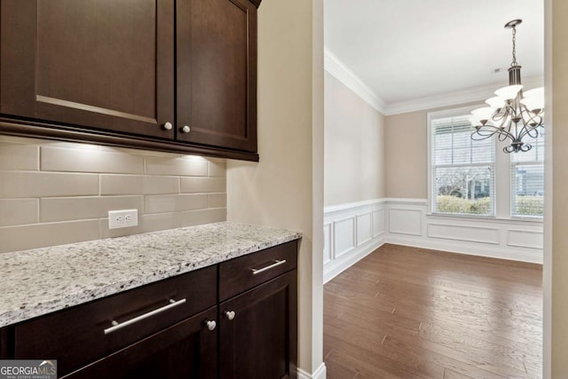 kitchen with an inviting chandelier, decorative light fixtures, dark brown cabinets, light stone countertops, and crown molding