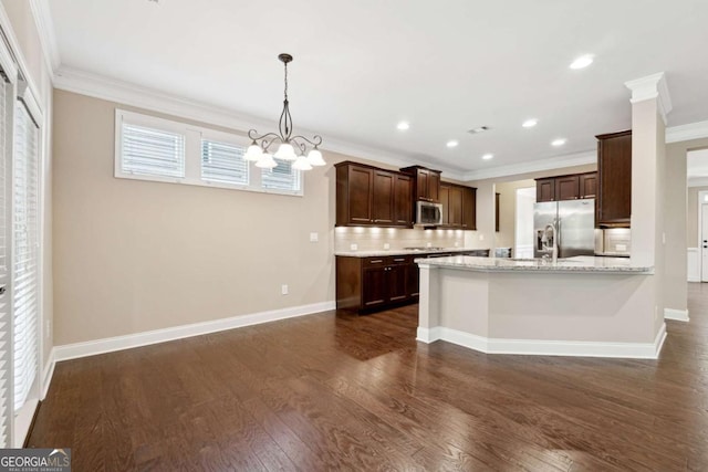 kitchen with light stone countertops, appliances with stainless steel finishes, decorative light fixtures, backsplash, and a chandelier