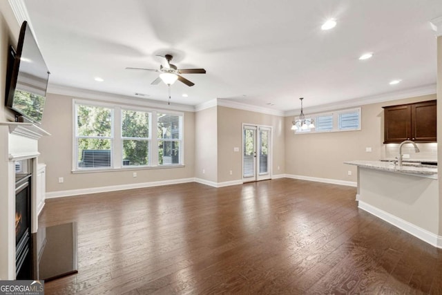 unfurnished living room featuring a fireplace, sink, ornamental molding, dark hardwood / wood-style flooring, and ceiling fan with notable chandelier