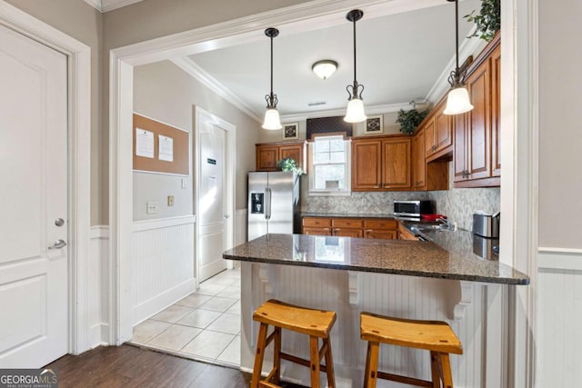 kitchen featuring kitchen peninsula, stainless steel refrigerator with ice dispenser, crown molding, pendant lighting, and a breakfast bar