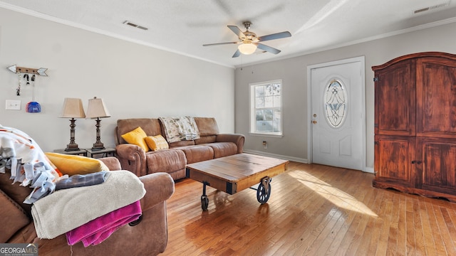 living room with ceiling fan, a textured ceiling, ornamental molding, and light wood-type flooring