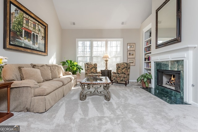 living room featuring lofted ceiling, built in shelves, a high end fireplace, and carpet flooring