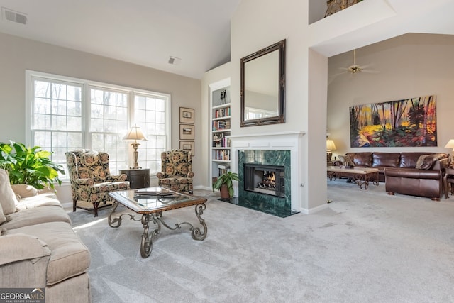 living room with built in features, ceiling fan, a fireplace, vaulted ceiling, and light colored carpet