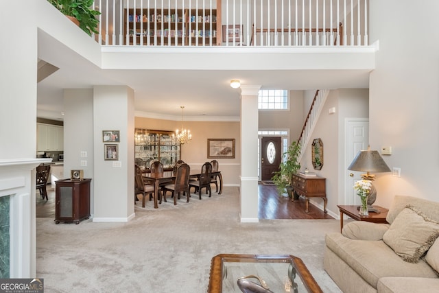 carpeted living room featuring an inviting chandelier, ornamental molding, ornate columns, and a high ceiling