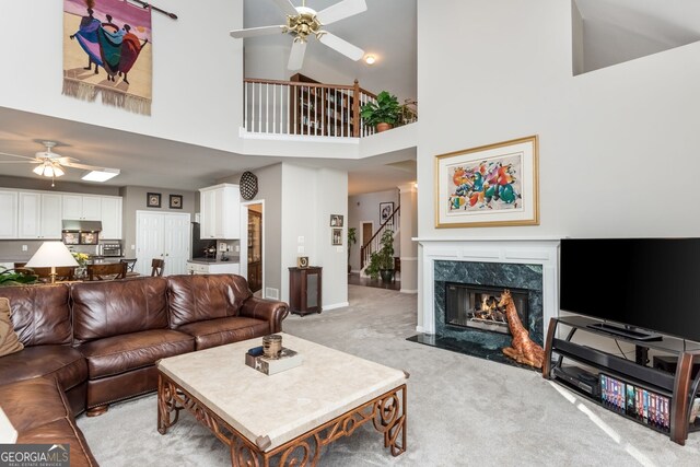 carpeted living room with ceiling fan, a towering ceiling, and a high end fireplace