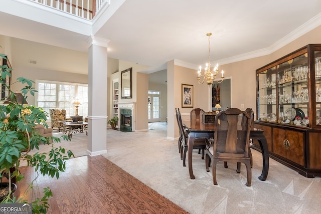 carpeted dining space with ornate columns, ornamental molding, a notable chandelier, and a fireplace