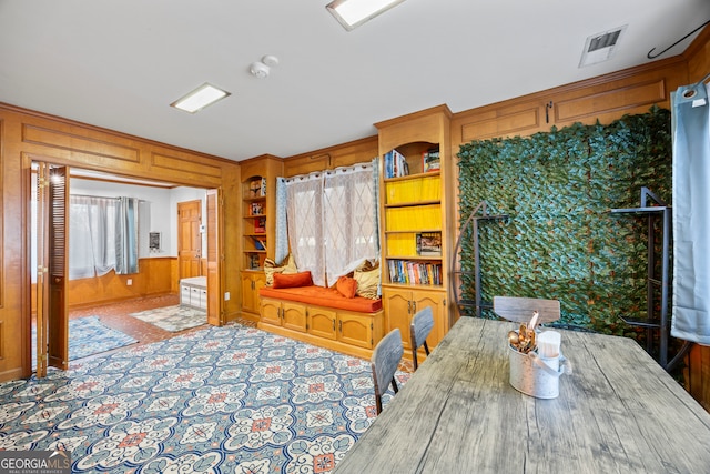 dining area with light carpet, built in shelves, wood walls, and visible vents