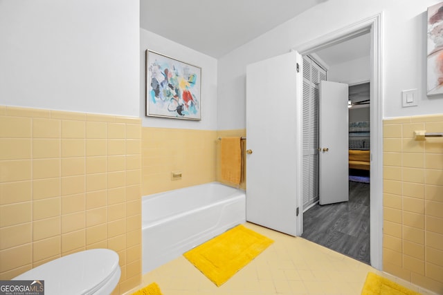 full bathroom featuring a wainscoted wall, tile walls, toilet, ensuite bathroom, and a bath