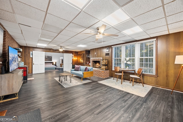 living area featuring ceiling fan, a brick fireplace, dark wood finished floors, and wooden walls