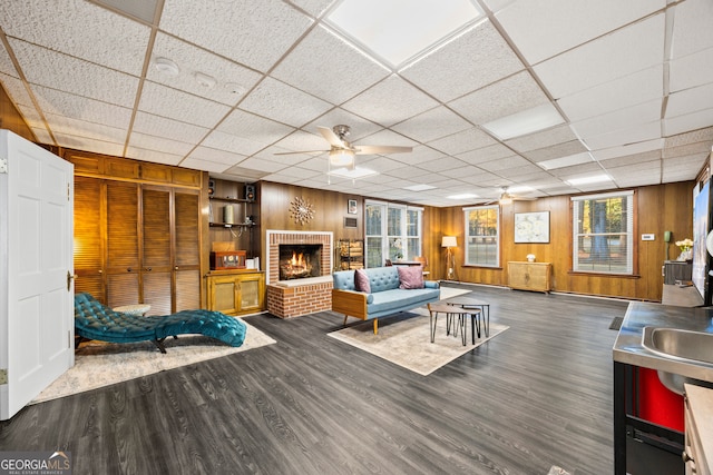 living room with dark wood finished floors, a fireplace, wood walls, and ceiling fan