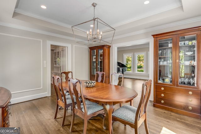 dining room with an inviting chandelier, ornamental molding, light hardwood / wood-style floors, and a raised ceiling