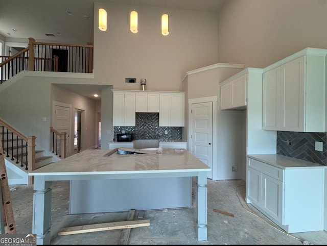 kitchen with a towering ceiling, white cabinetry, tasteful backsplash, and decorative light fixtures