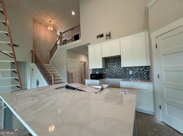 kitchen with white cabinetry, a towering ceiling, light stone counters, an inviting chandelier, and decorative backsplash