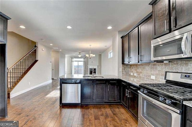 kitchen with decorative light fixtures, light stone countertops, kitchen peninsula, and stainless steel appliances