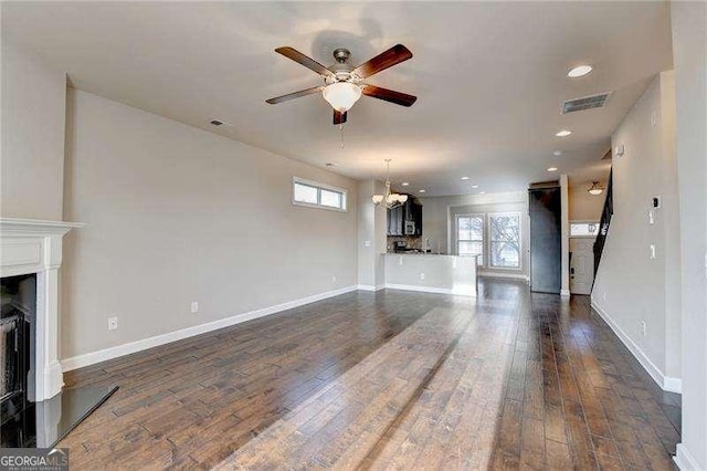 unfurnished living room with a healthy amount of sunlight, dark hardwood / wood-style flooring, and ceiling fan with notable chandelier