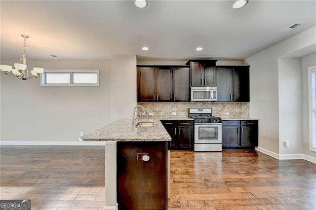 kitchen featuring backsplash, kitchen peninsula, sink, light stone countertops, and appliances with stainless steel finishes