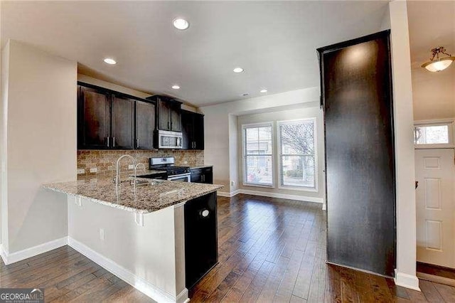 kitchen with light stone countertops, appliances with stainless steel finishes, sink, backsplash, and a breakfast bar area