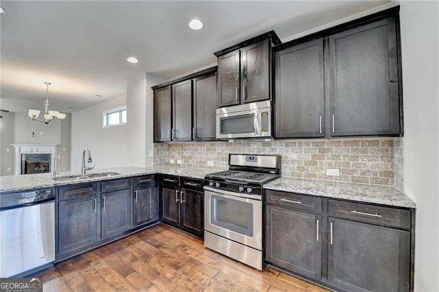 kitchen with light stone countertops, appliances with stainless steel finishes, dark wood-type flooring, sink, and a chandelier