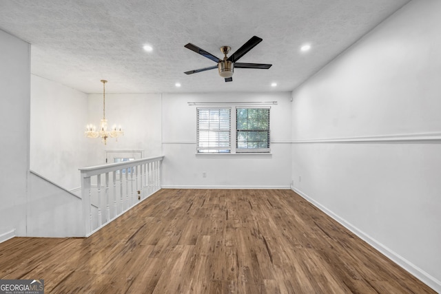 empty room featuring hardwood / wood-style flooring, ceiling fan with notable chandelier, and a textured ceiling