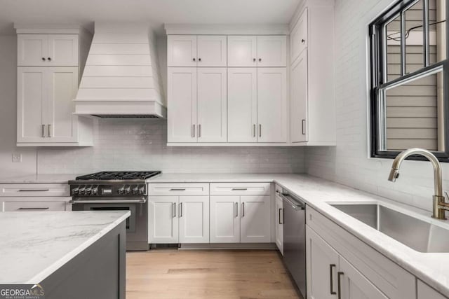 kitchen with custom exhaust hood, white cabinets, sink, and stainless steel appliances