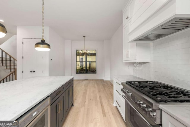 kitchen featuring decorative light fixtures, light stone counters, premium range hood, and white cabinetry