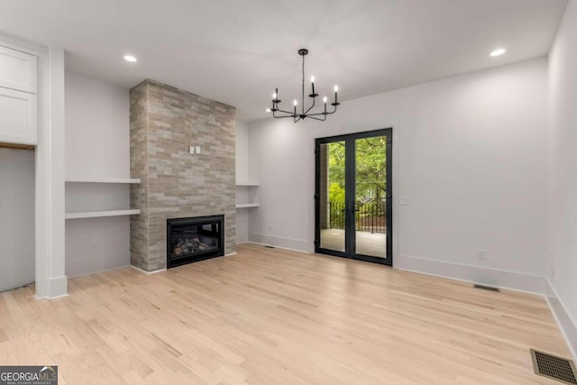 unfurnished living room featuring built in shelves, french doors, a large fireplace, a notable chandelier, and light hardwood / wood-style flooring