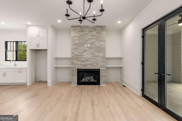 unfurnished living room featuring built in shelves, light wood-type flooring, a fireplace, and sink