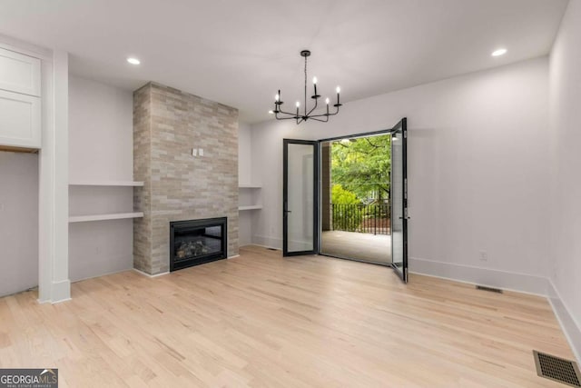 unfurnished living room with light wood-type flooring, built in features, a chandelier, and a fireplace