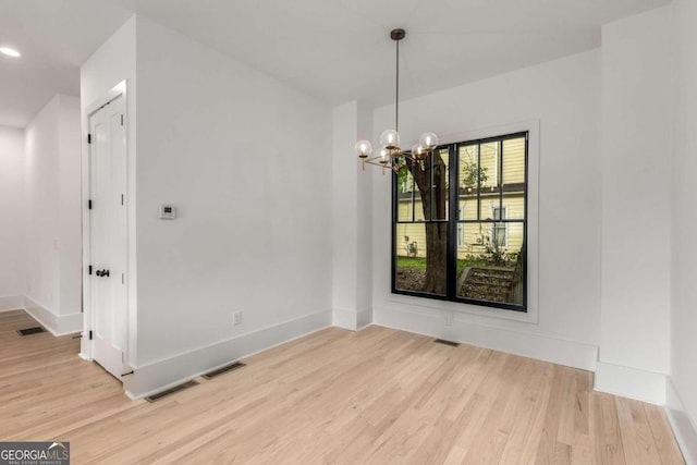 unfurnished dining area featuring an inviting chandelier and light hardwood / wood-style floors