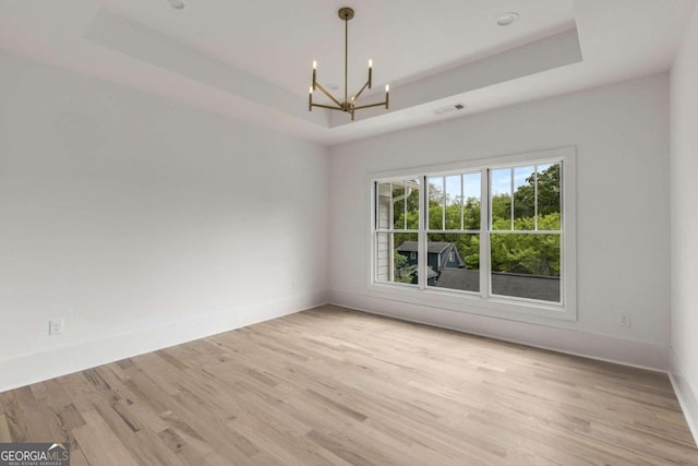 empty room featuring a raised ceiling, a notable chandelier, and light hardwood / wood-style floors