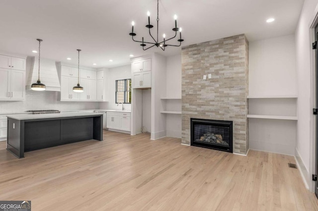 kitchen with pendant lighting, white cabinets, a kitchen island, premium range hood, and a tile fireplace