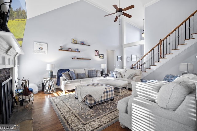 living room with crown molding, dark wood-type flooring, ceiling fan, a high ceiling, and a stone fireplace