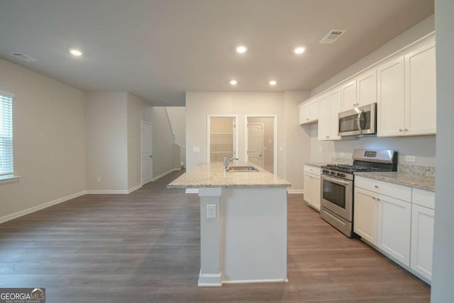 kitchen featuring white cabinets, appliances with stainless steel finishes, an island with sink, and light stone counters