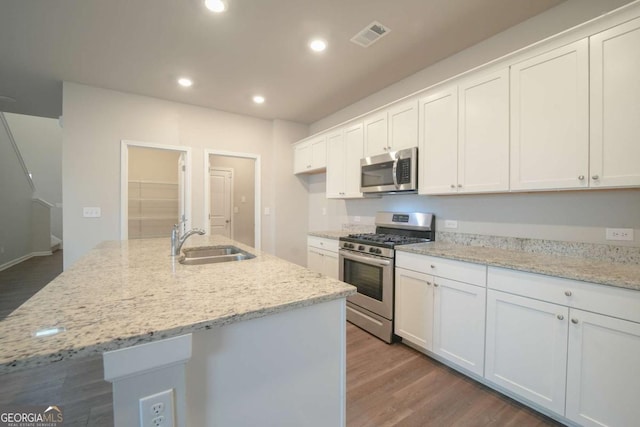 kitchen with a center island with sink, sink, white cabinetry, stainless steel appliances, and light stone counters