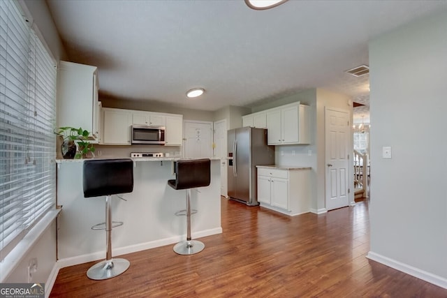 kitchen with dark hardwood / wood-style floors, a breakfast bar area, stainless steel appliances, and white cabinets