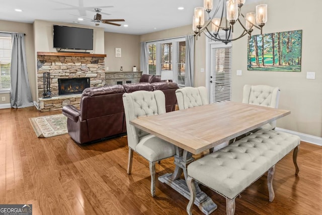 dining room with ceiling fan with notable chandelier, a fireplace, and wood-type flooring