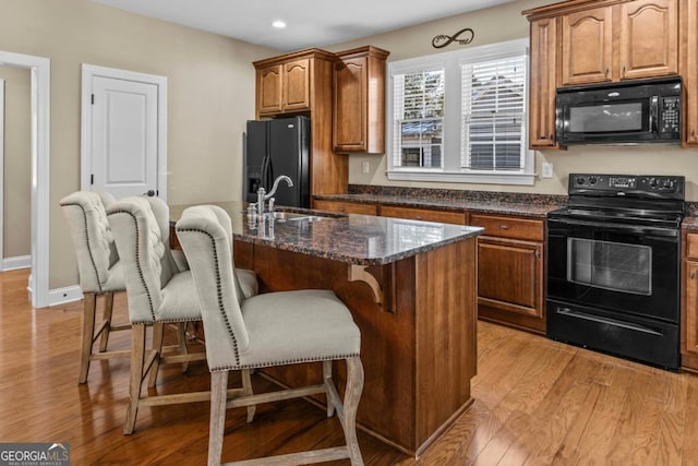 kitchen featuring a kitchen breakfast bar, a kitchen island with sink, dark stone counters, and black appliances