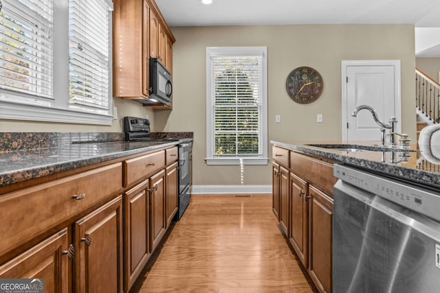 kitchen featuring sink, light hardwood / wood-style flooring, black appliances, and dark stone countertops