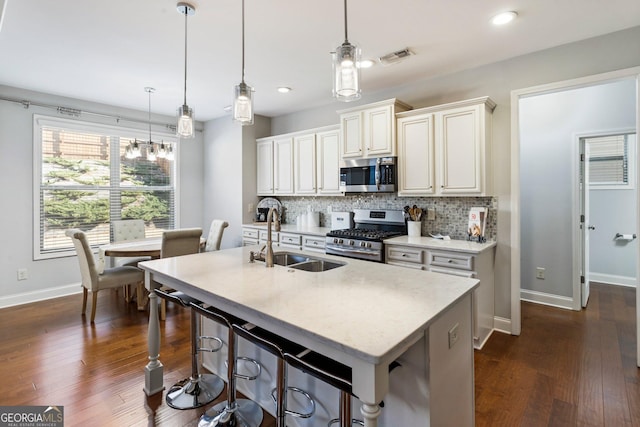 kitchen with an island with sink, stainless steel appliances, backsplash, hanging light fixtures, and sink