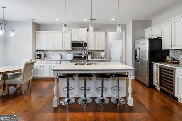 kitchen with wine cooler, white cabinetry, hanging light fixtures, a kitchen island with sink, and appliances with stainless steel finishes