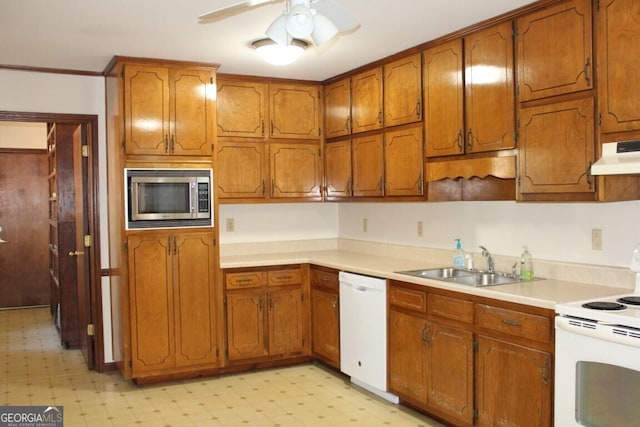 kitchen with light floors, brown cabinetry, a sink, white appliances, and under cabinet range hood