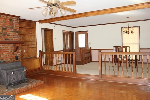 living room with ceiling fan with notable chandelier, wood finished floors, visible vents, a wood stove, and crown molding