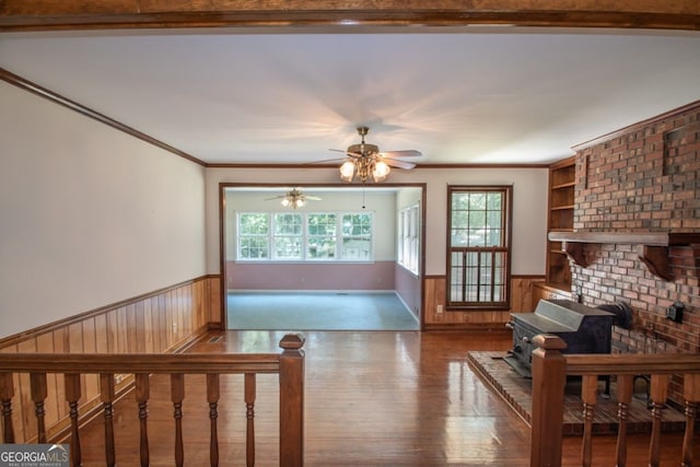 unfurnished living room featuring a wealth of natural light, a wainscoted wall, crown molding, and wooden walls