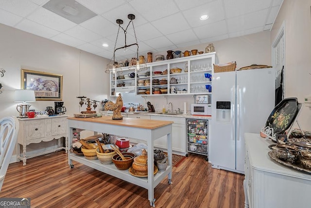 kitchen with a drop ceiling, white appliances, white cabinetry, hanging light fixtures, and dark hardwood / wood-style flooring