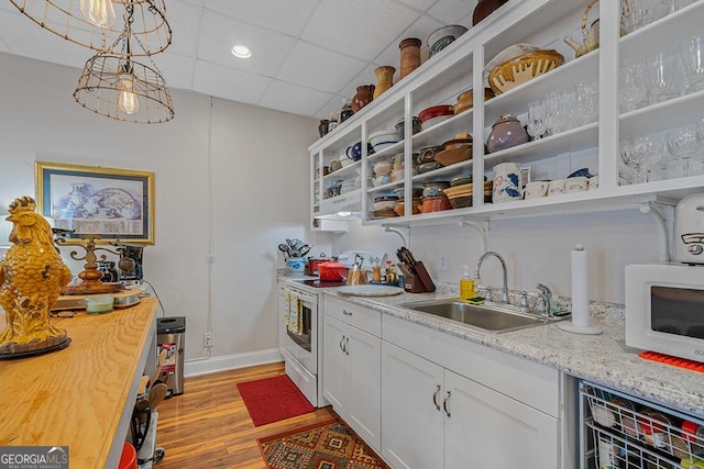 kitchen with sink, white appliances, hanging light fixtures, a paneled ceiling, and white cabinets