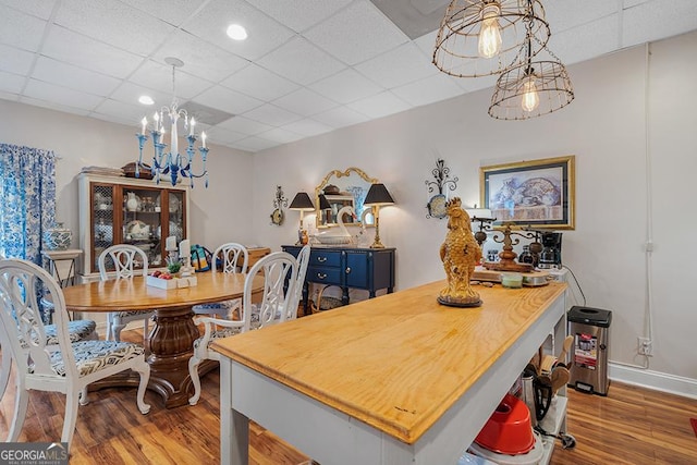 dining room with a drop ceiling, light hardwood / wood-style flooring, and an inviting chandelier