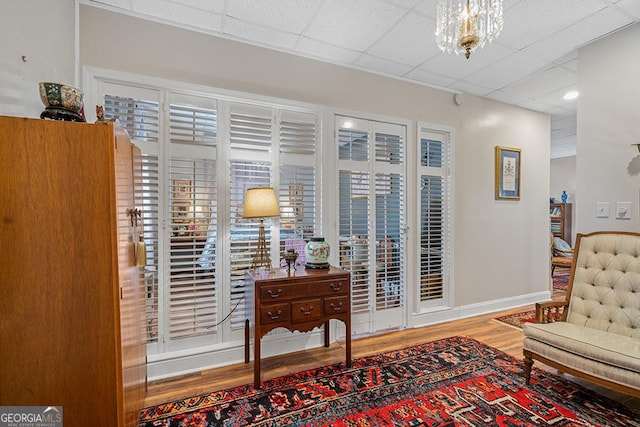 living area with an inviting chandelier, hardwood / wood-style floors, and a drop ceiling