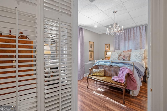 bedroom with a drop ceiling, a chandelier, and hardwood / wood-style floors